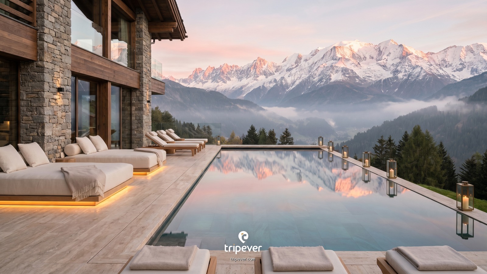 An infinity pool at a stone-and-timber alpine resort overlooks misty pine-covered mountains and distant snow-capped peaks at dawn